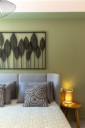Een bed met beddengoed met een patroon, een wandkunst van een blad en een nachtkastje met een lamp.