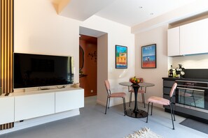 Een moderne woonkamer met een flatscreen televisie, een eethoek met een ronde tafel en stoelen, en een keuken met een inbouwoven.