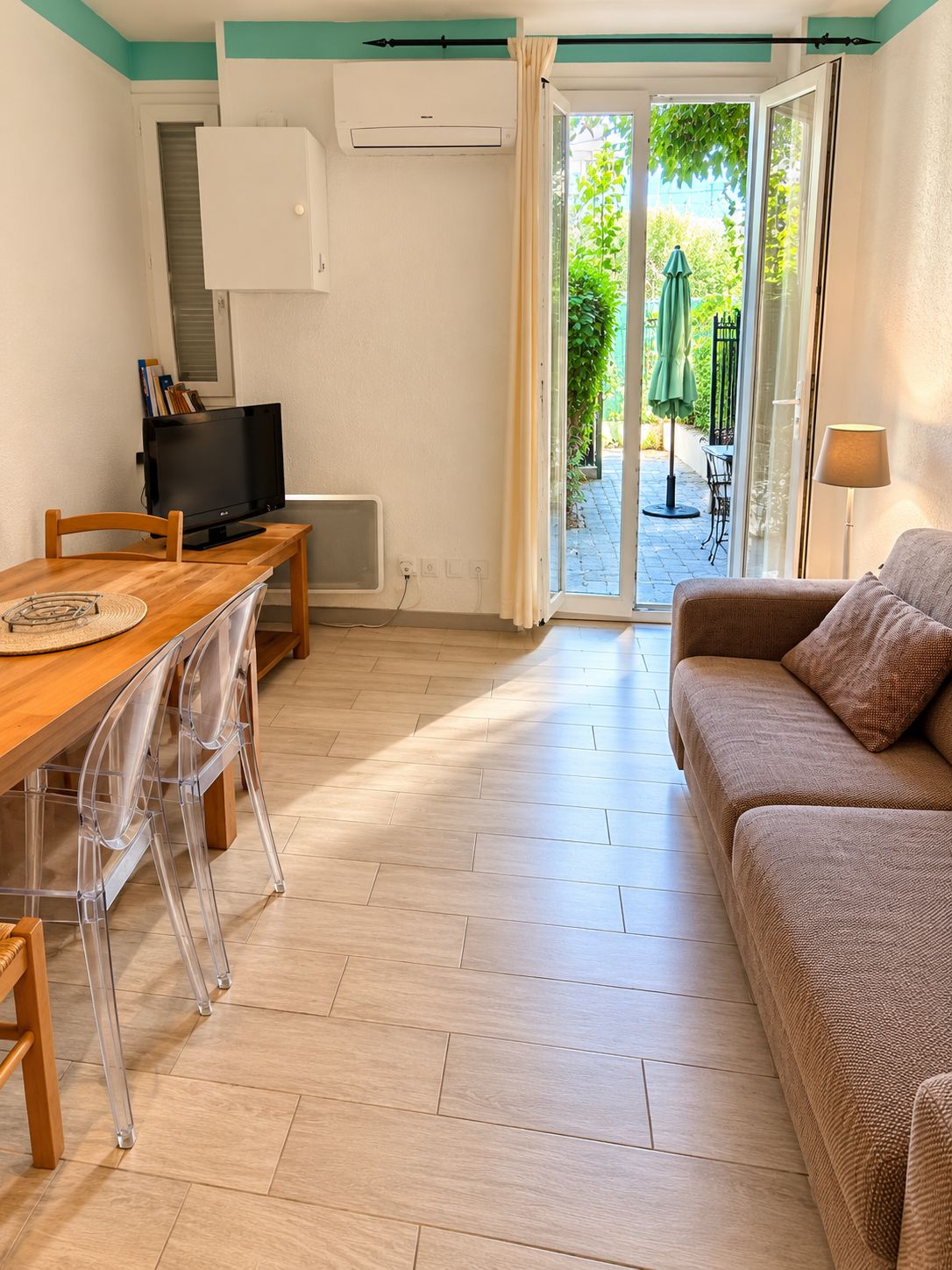 Un espace de vie compact comprenant une table à manger en bois, un canapé, un téléviseur et une porte-fenêtre coulissante donnant sur un espace extérieur.