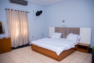 Un dormitorio con cama, mesita de noche, aire acondicionado de pared y cortina.