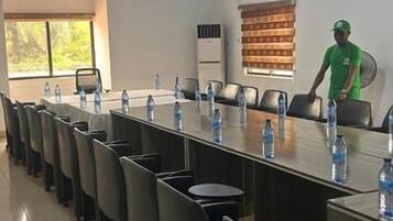 A conference room with a long table, chairs, water bottles, and a person in a green shirt standing by the window.