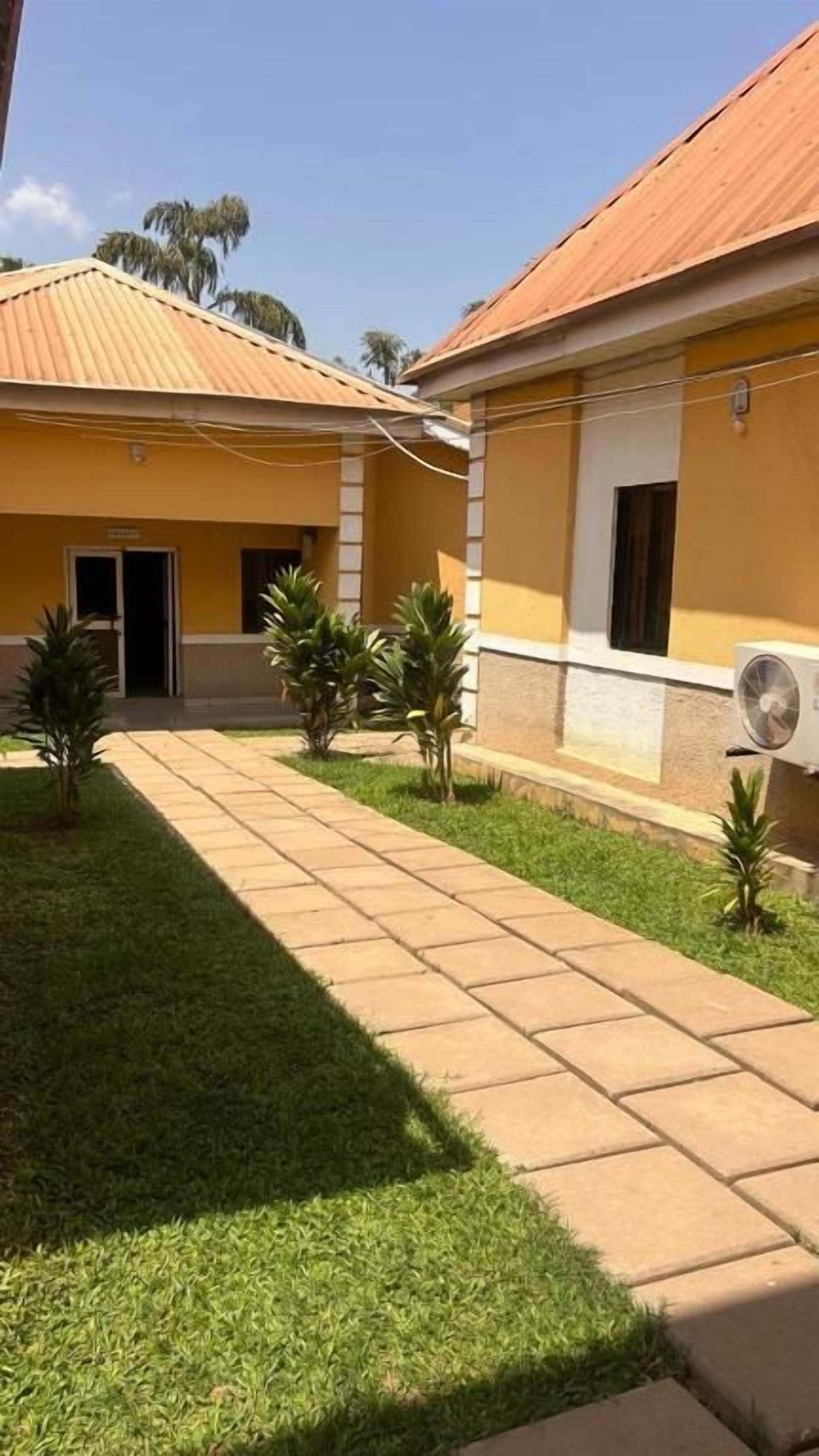 Une cour avec un chemin pavé, de petits palmiers et un bâtiment doté d’un toit en tuiles.