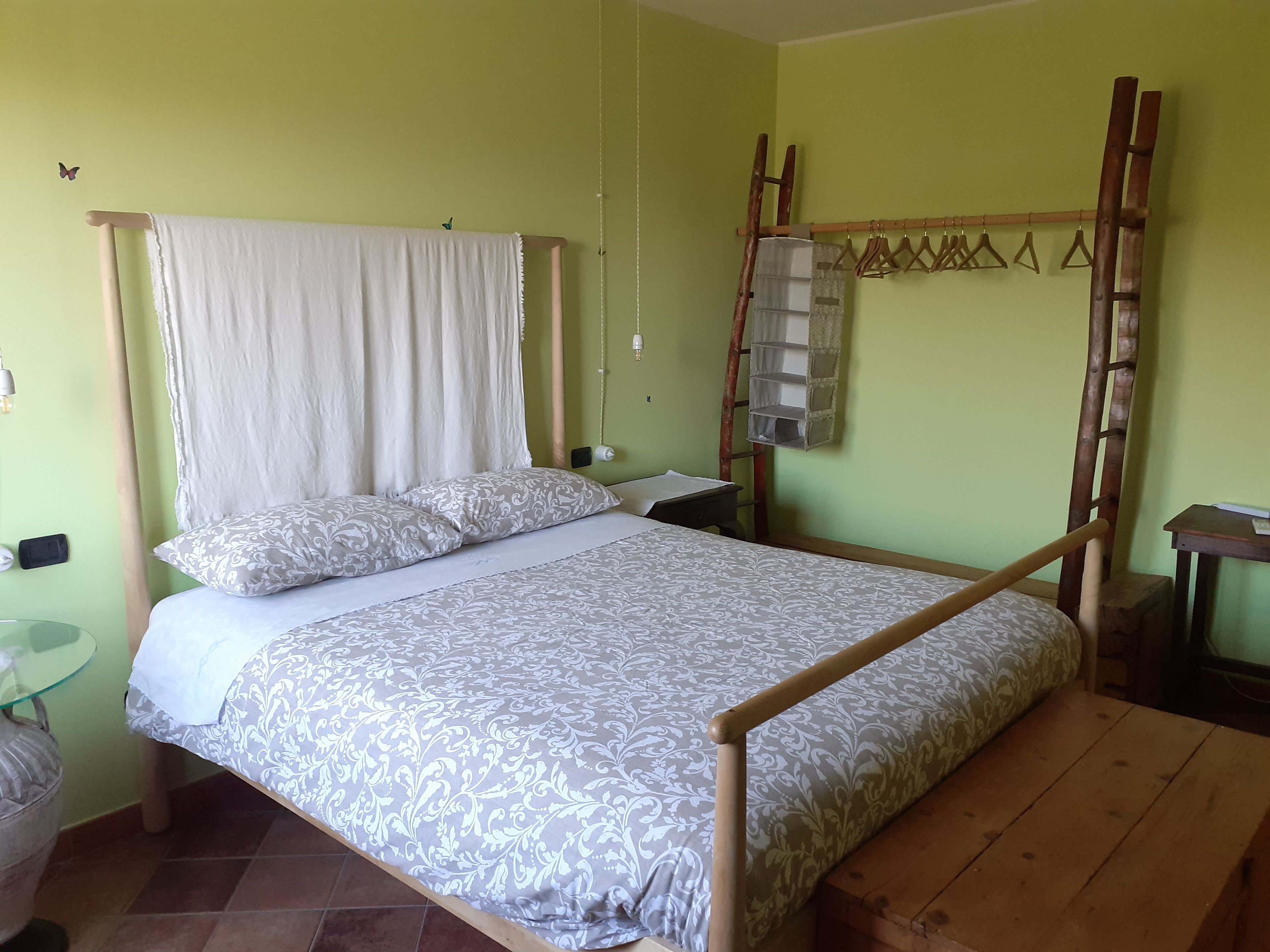 A single bed with a wooden frame and a canopy, a bedside table, a wall-mounted shelf, and a small table with a lamp.