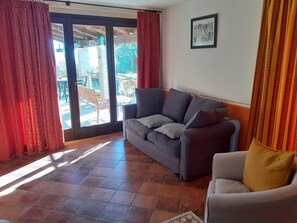 Un salon comprenant un canapé, un fauteuil, un sol carrelé et une porte-fenêtre coulissante donnant sur un espace extérieur.