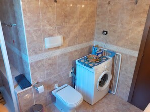 Un baño pequeño con inodoro, lavadora y zona de ducha.