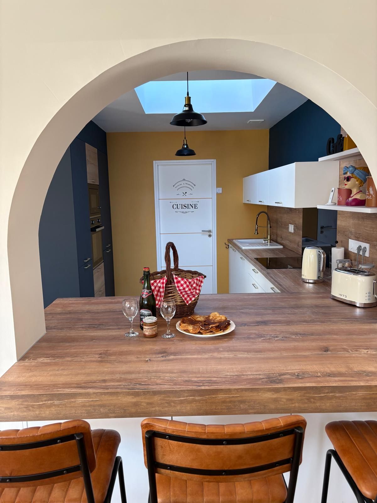 Un coin repas avec une table en bois, des chaises, une bouteille de bière, des verres et un panier.