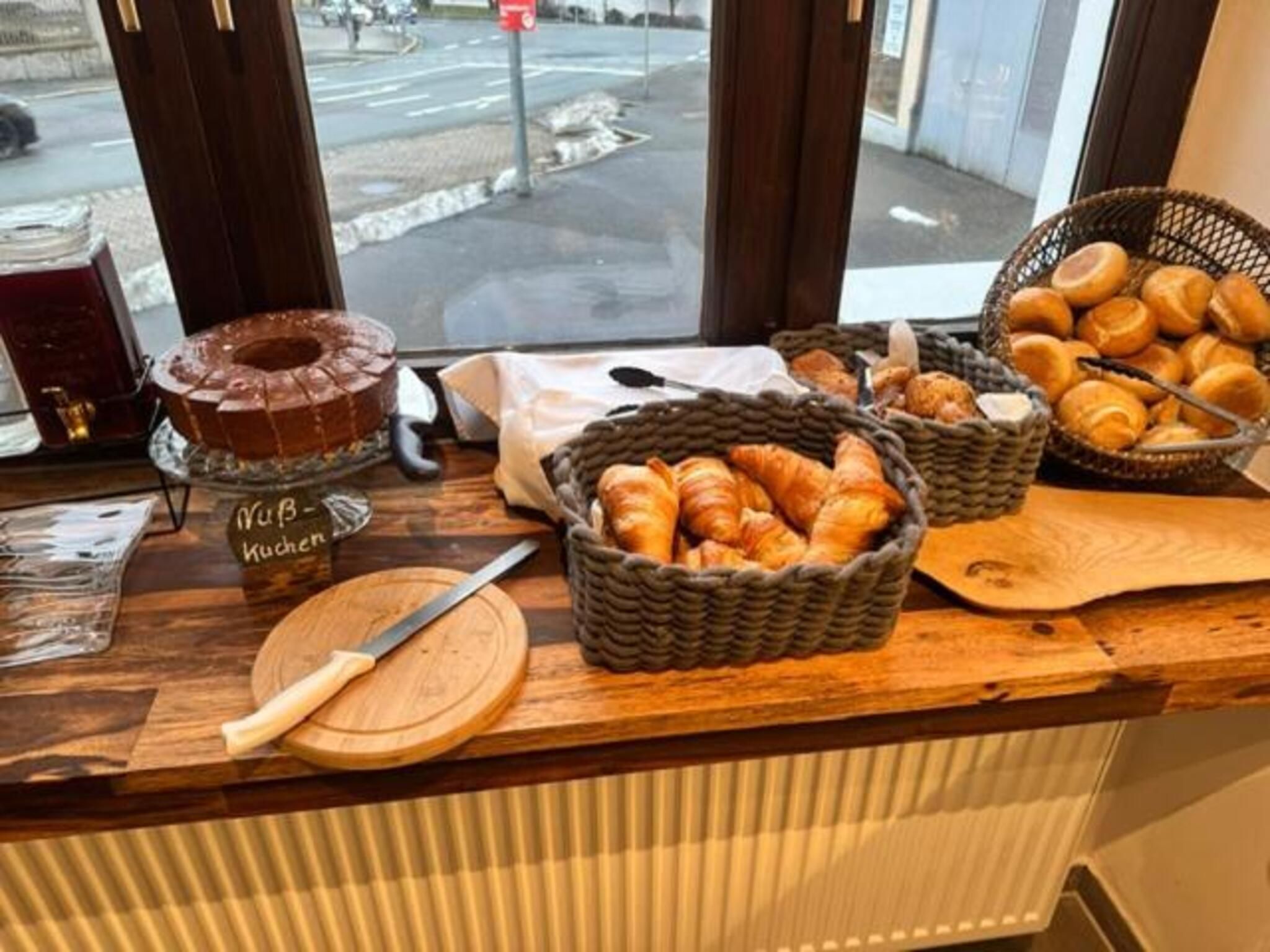 A bakery counter with a cake, croissants, and a knife on a wooden surface.