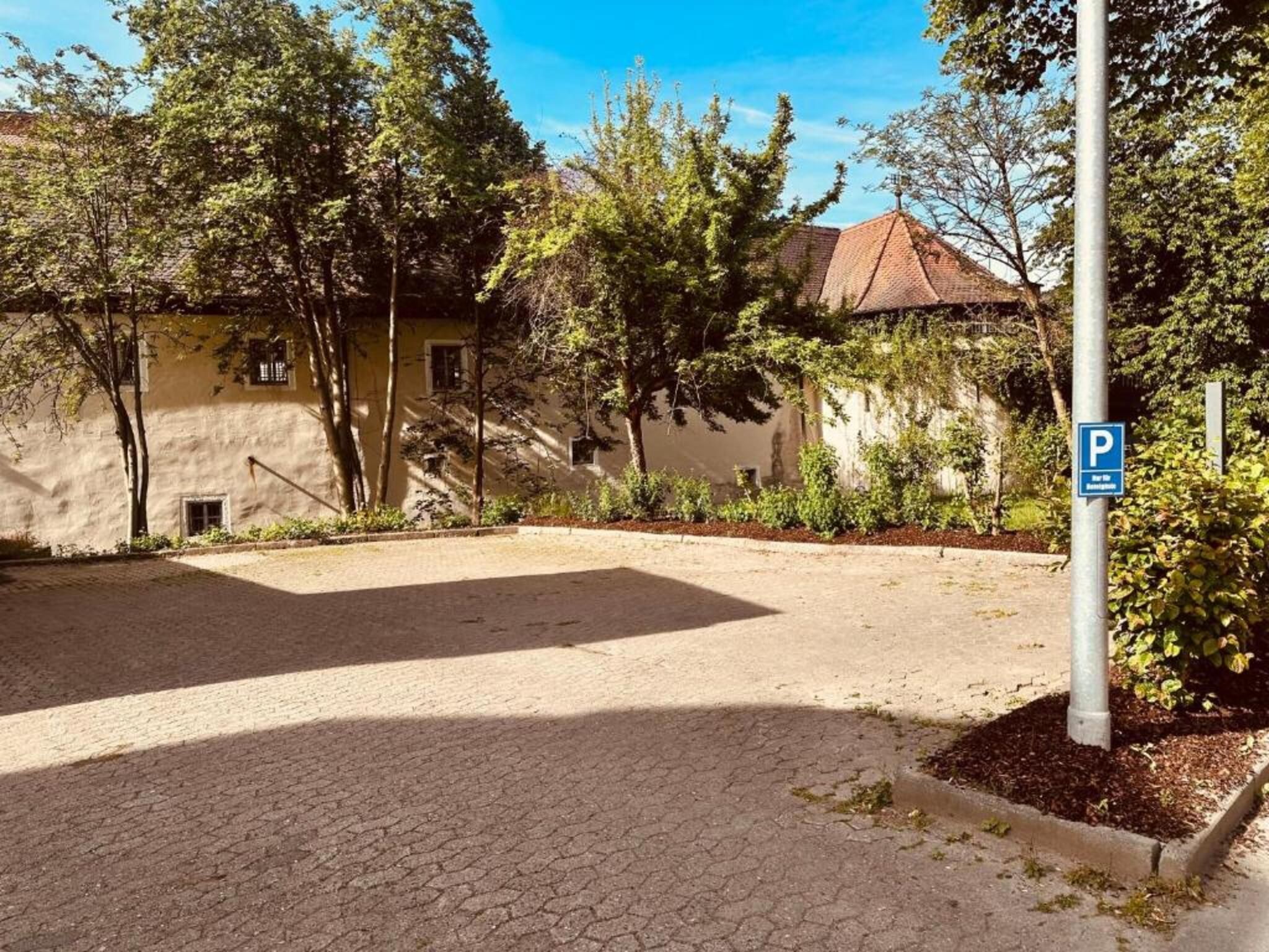 Ein gepflasterter Innenhof mit Parkschild, umgeben von Bäumen und einem Gebäude mit einem Ziegeldach.
