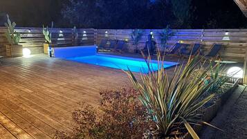 Une terrasse en bois avec une piscine, entourée de plantes et de chaises.
