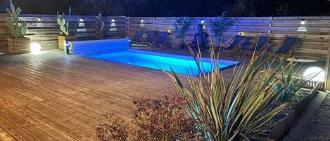 A wooden deck with a swimming pool, surrounded by plants and chairs.