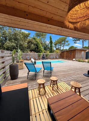 Une terrasse extérieure avec une piscine, des meubles en bois et un toit de chaume.