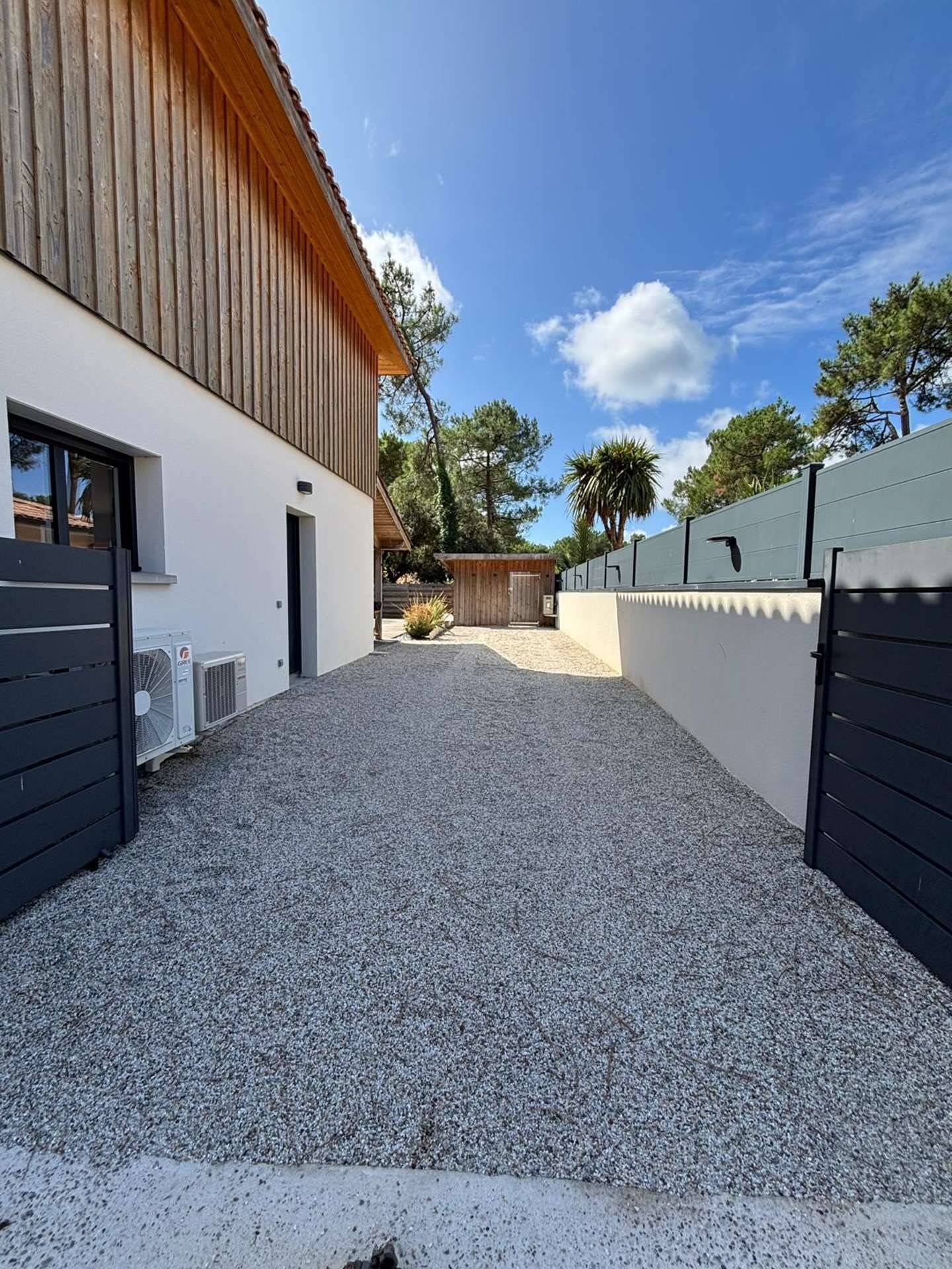 Un bâtiment moderne avec une allée de gravier menant à un portail en bois.