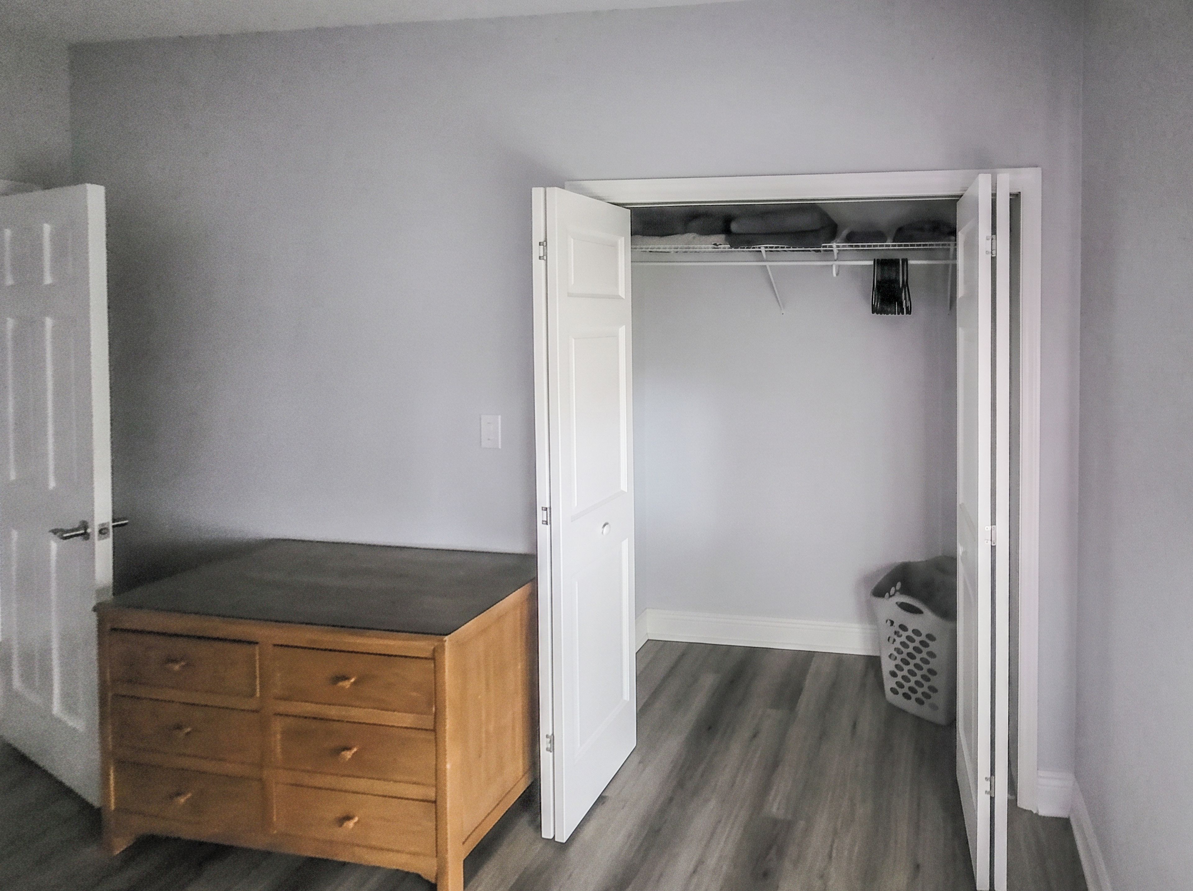 A room with a wooden dresser, a closet with open doors, and a laundry basket.