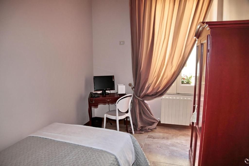 A bedroom with a bed, a desk with a computer, a chair, and a window with curtains.