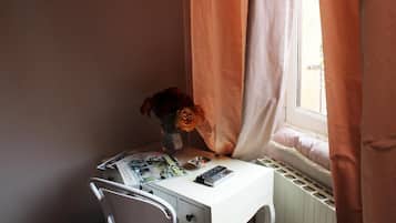 A small desk with a chair, a vase with flowers, a magazine, and a remote control.