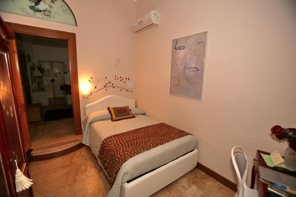 Un dormitorio con una cama, un escritorio, una silla, un aire acondicionado y una obra de arte en la pared.