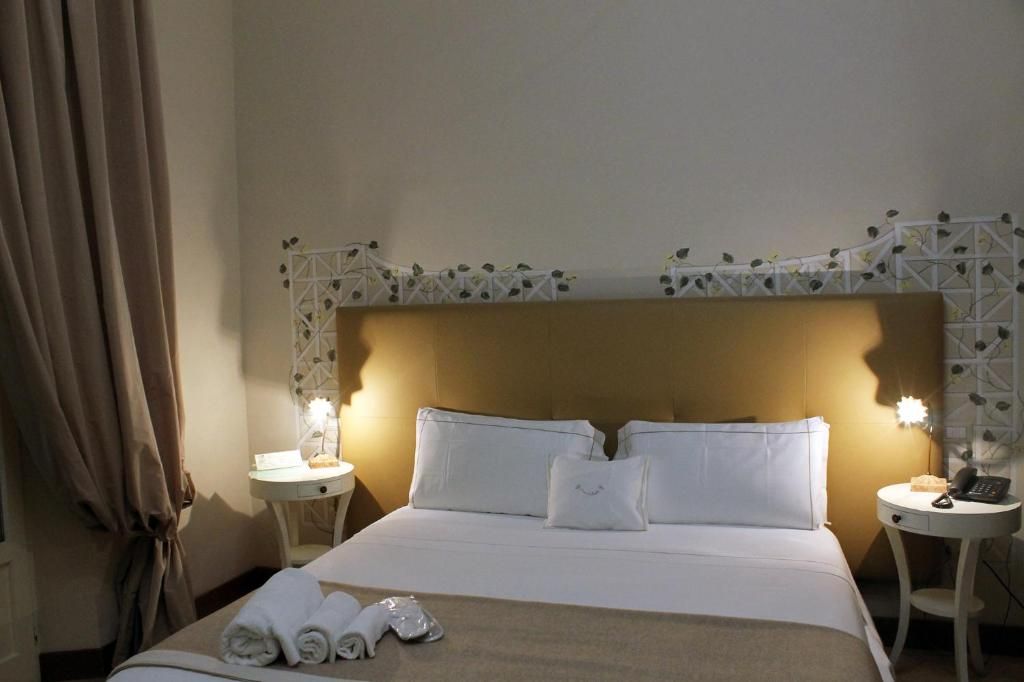 Habitación de hotel con una cama grande, dos mesitas de noche, un cabecero con un diseño decorativo y una cortina a la izquierda.