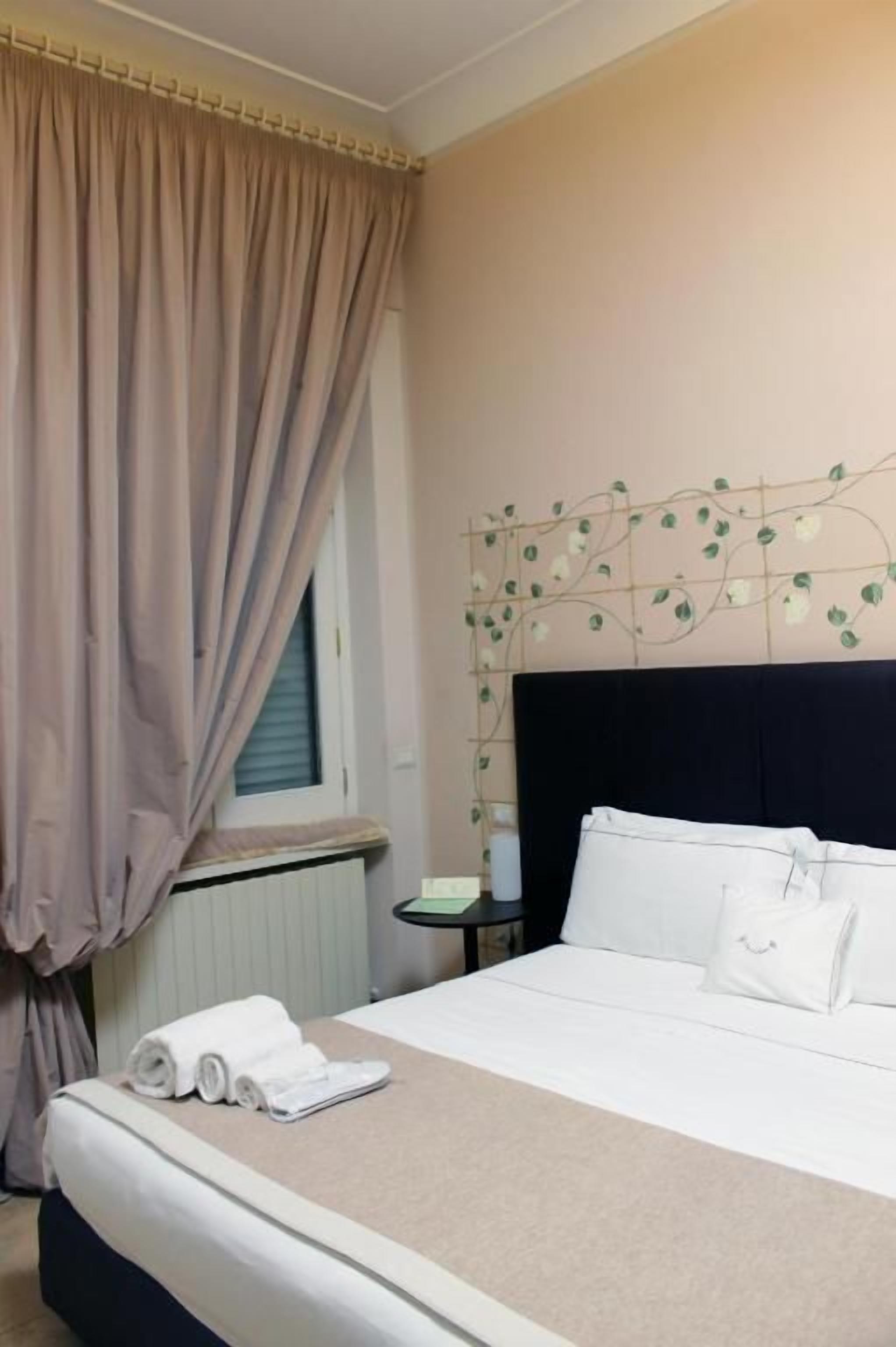 Ein Hotelzimmer mit einem Bett, einem Nachttisch, einem Fenster mit Vorhängen und einer Wanddekoration.