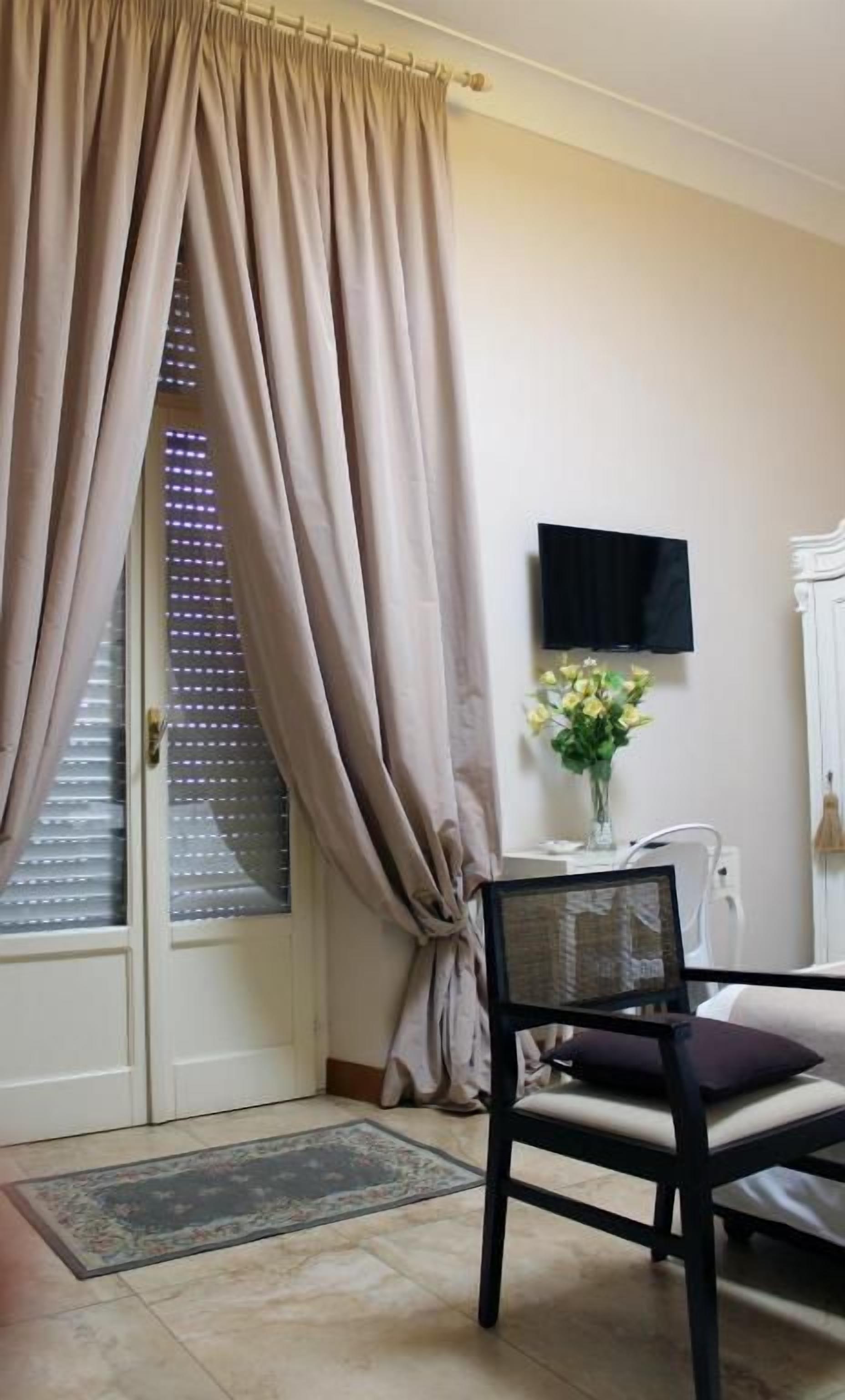 Une pièce comprenant un lit, une chaise, un téléviseur et une fenêtre avec des rideaux.