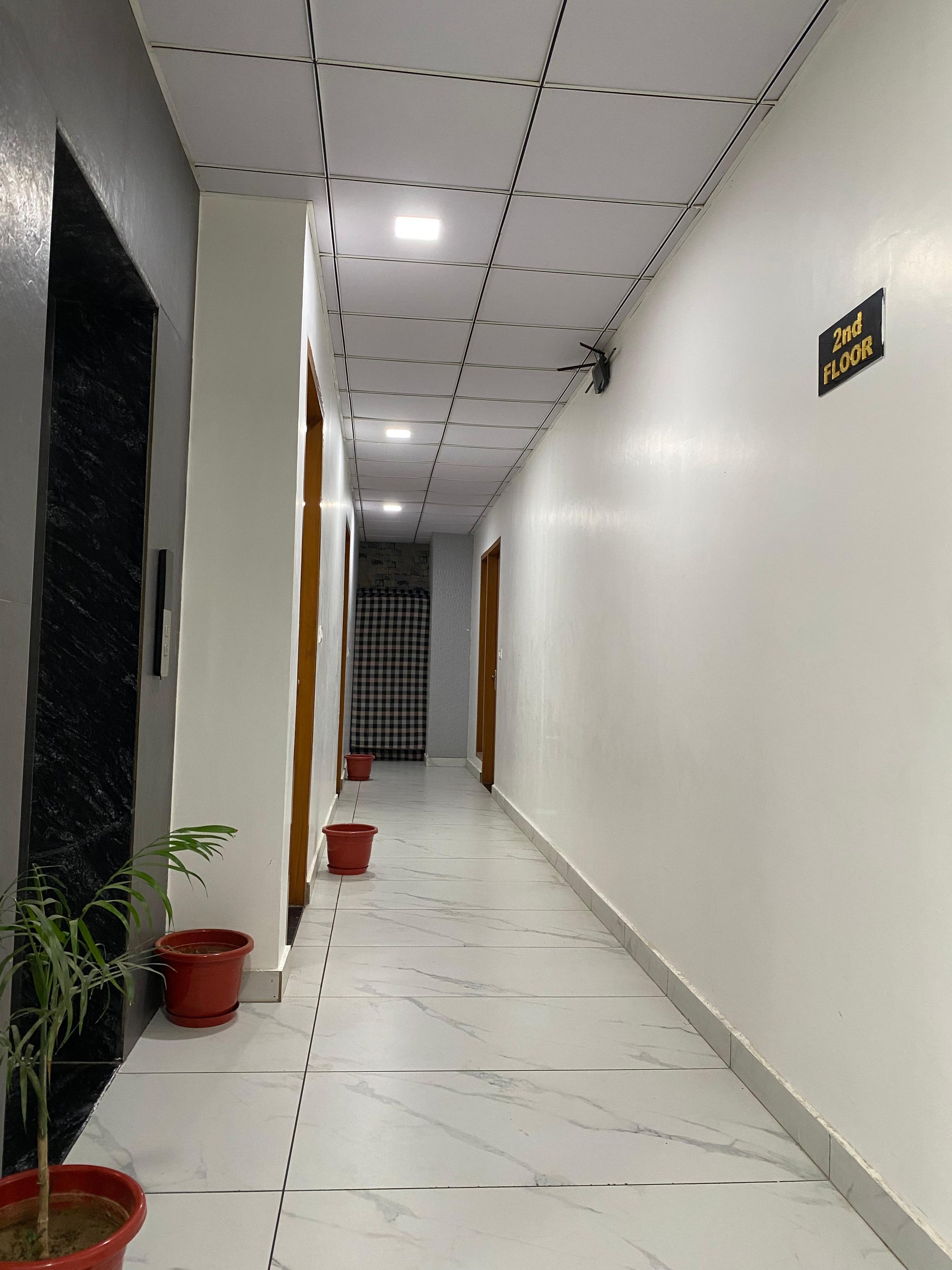 A hallway with a '2nd FLOOR' sign, potted plants, and a checkered curtain at the end.