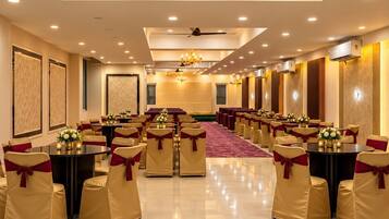 A banquet hall with round tables, chairs with red sashes, a patterned ceiling, and recessed lighting.
