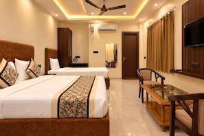 A hotel room with two beds, a desk, a chair, a ceiling fan, an air conditioning unit, and a television on the wall.