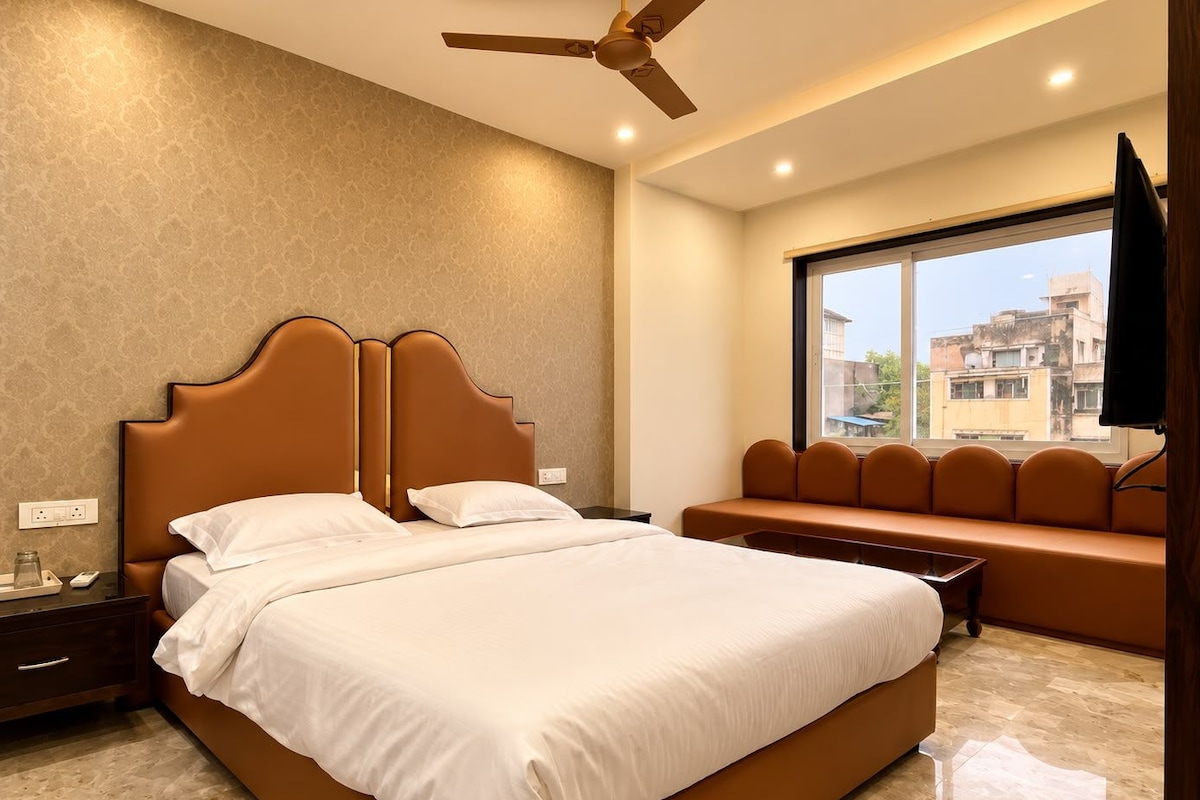 Une chambre d’hôtel avec un grand lit, un ventilateur de plafond, une fenêtre donnant sur la ville et un banc près de la fenêtre.