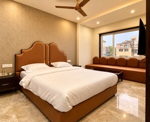 Une chambre d’hôtel avec un grand lit, un ventilateur de plafond, une fenêtre donnant sur la ville et un banc près de la fenêtre.
