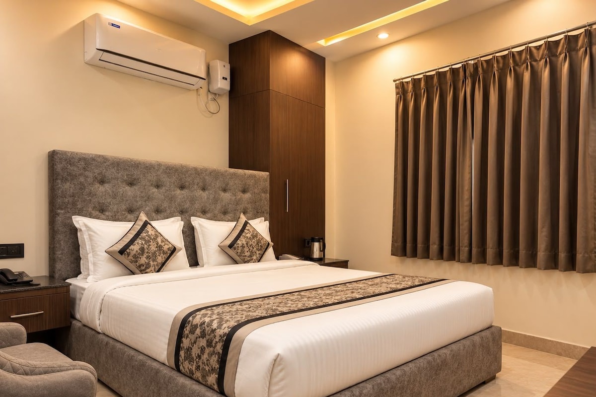 Une chambre d’hôtel avec un grand lit, une table de chevet, une commode, un canapé, un climatiseur, un radiateur mural et une fenêtre avec des rideaux.