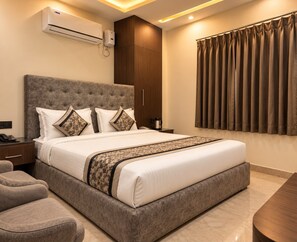 Une chambre d’hôtel avec un grand lit, une table de chevet, une commode, un canapé, un climatiseur, un radiateur mural et une fenêtre avec des rideaux.