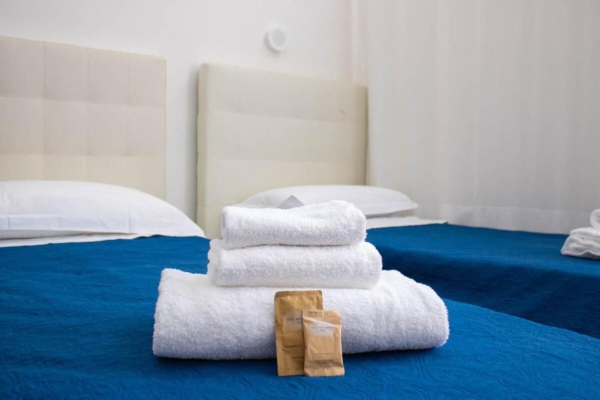 A hotel room with a bed, white pillows, a blue bedspread, and a stack of white towels.
