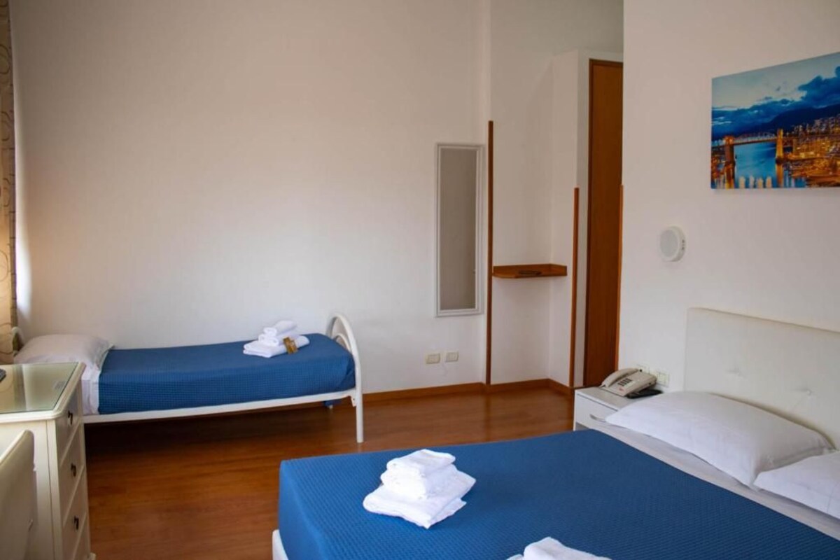 A hotel room with two beds, a desk, and a painting on the wall.