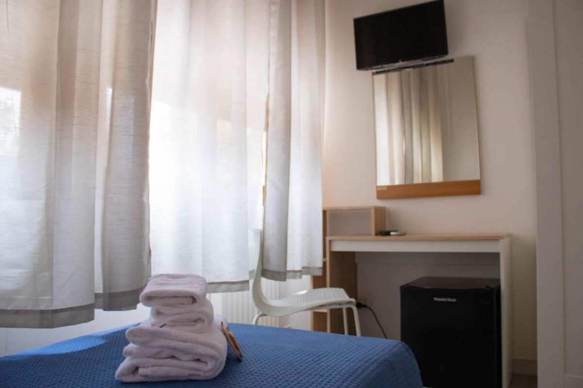 A hotel room with a bed, a desk, a chair, a television, and a radiator.