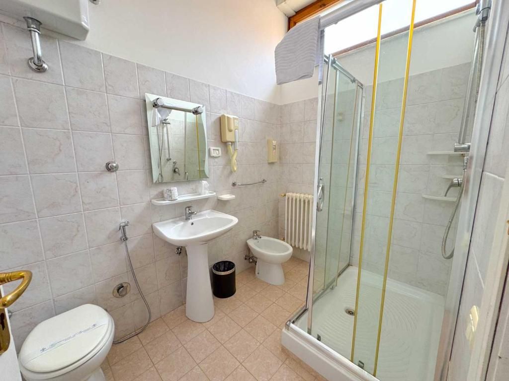 A bathroom with a toilet, bidet, sink, and a glass-enclosed shower area.