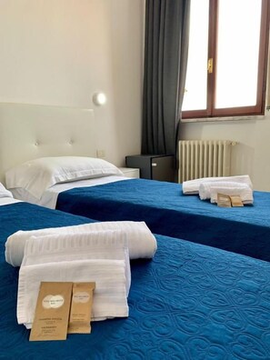 A hotel room with two beds, each with a blue bedspread and white linens. There are towels and toiletries on the beds. - Oasi San Francesco (Roma)