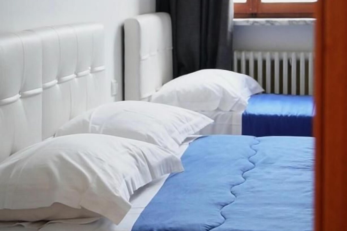 A bedroom with two beds, one with white bedding and the other with blue bedding, a white headboard, and a window with curtains.