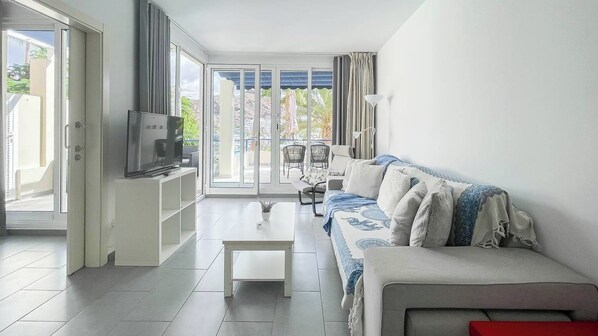 Un salón moderno con sofá, mesa de centro, televisor y balcón con vistas.