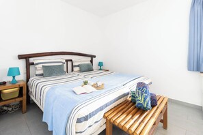 Una cama bien hecha con ropa de cama a rayas, una mesita de noche con una lámpara y un banco de madera con un cojín.