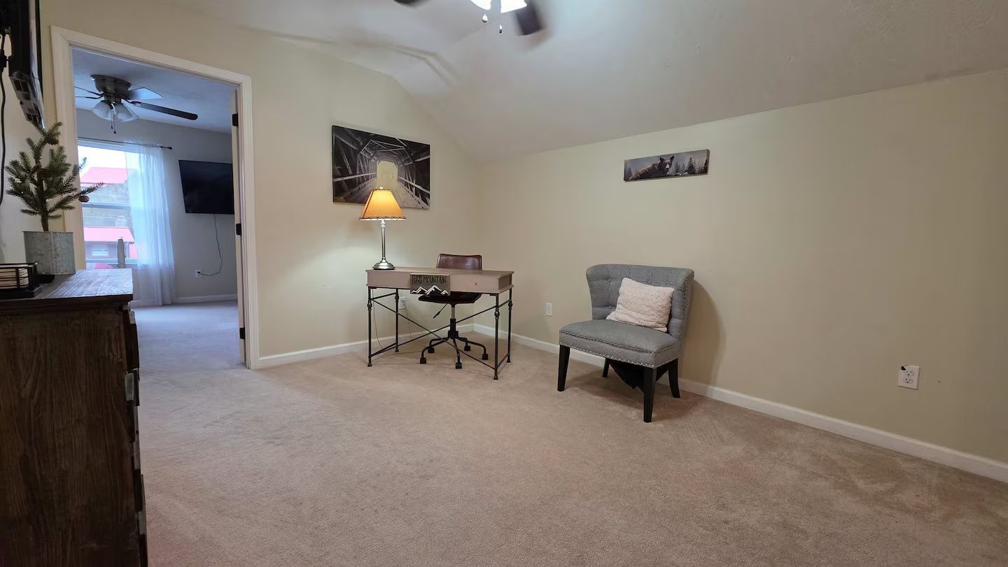 A carpeted room with a desk, office chair, and a standing lamp.