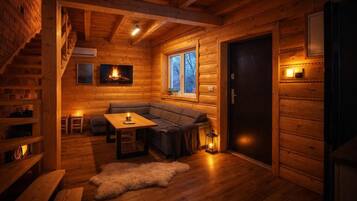 A cozy log cabin interior with a fireplace, a sofa, a table, and a window.