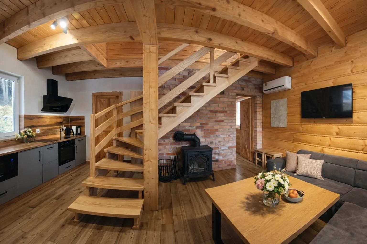 Een modern ingerichte blokhut met een houten trap, keuken, zithoek en een open haard.