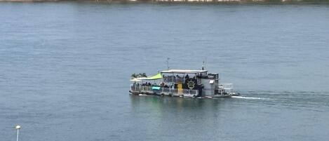 A riverboat with a covered deck and a flag, floating on a calm body of water.