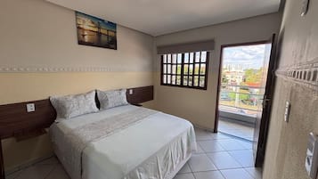 A hotel room with a bed, a window with blinds, a painting on the wall, and a view of the outside.