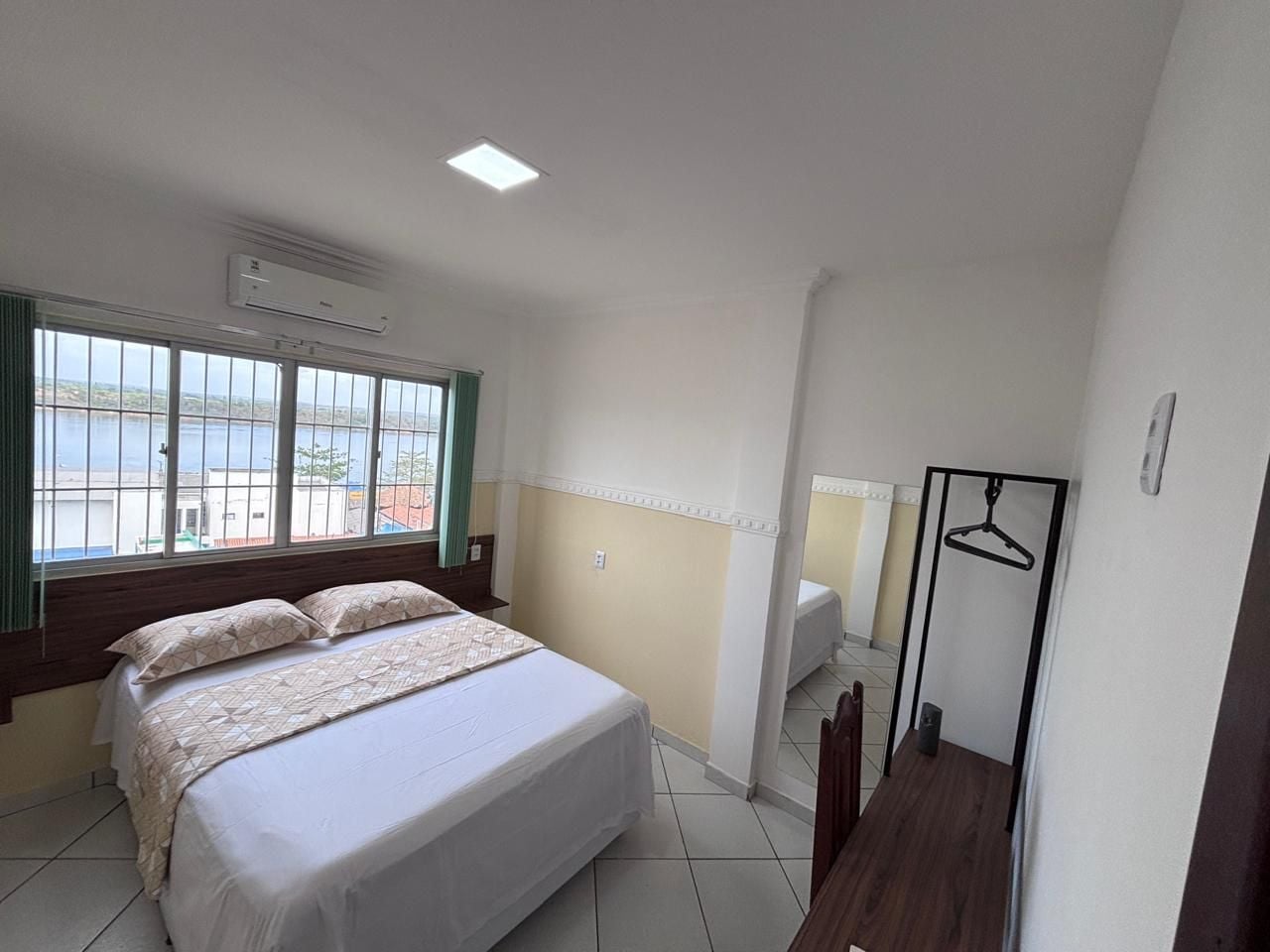 A hotel room with a bed, a desk, a chair, a hanging clothes rack, and a window with a view.