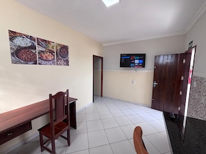 Habitació d'hotel amb zona de menjador, televisió penjada a la paret i una porta amb un número.