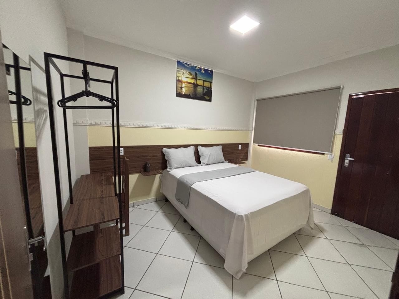 A bedroom with a bed, a wooden table, a hanging rack, and a window.