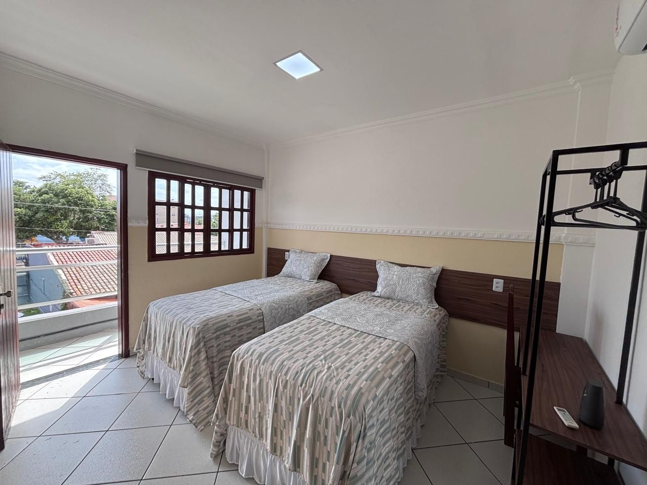 Habitación de hotel con dos camas, una ventana que da al exterior, una lámpara en el techo y una mesita con un altavoz.