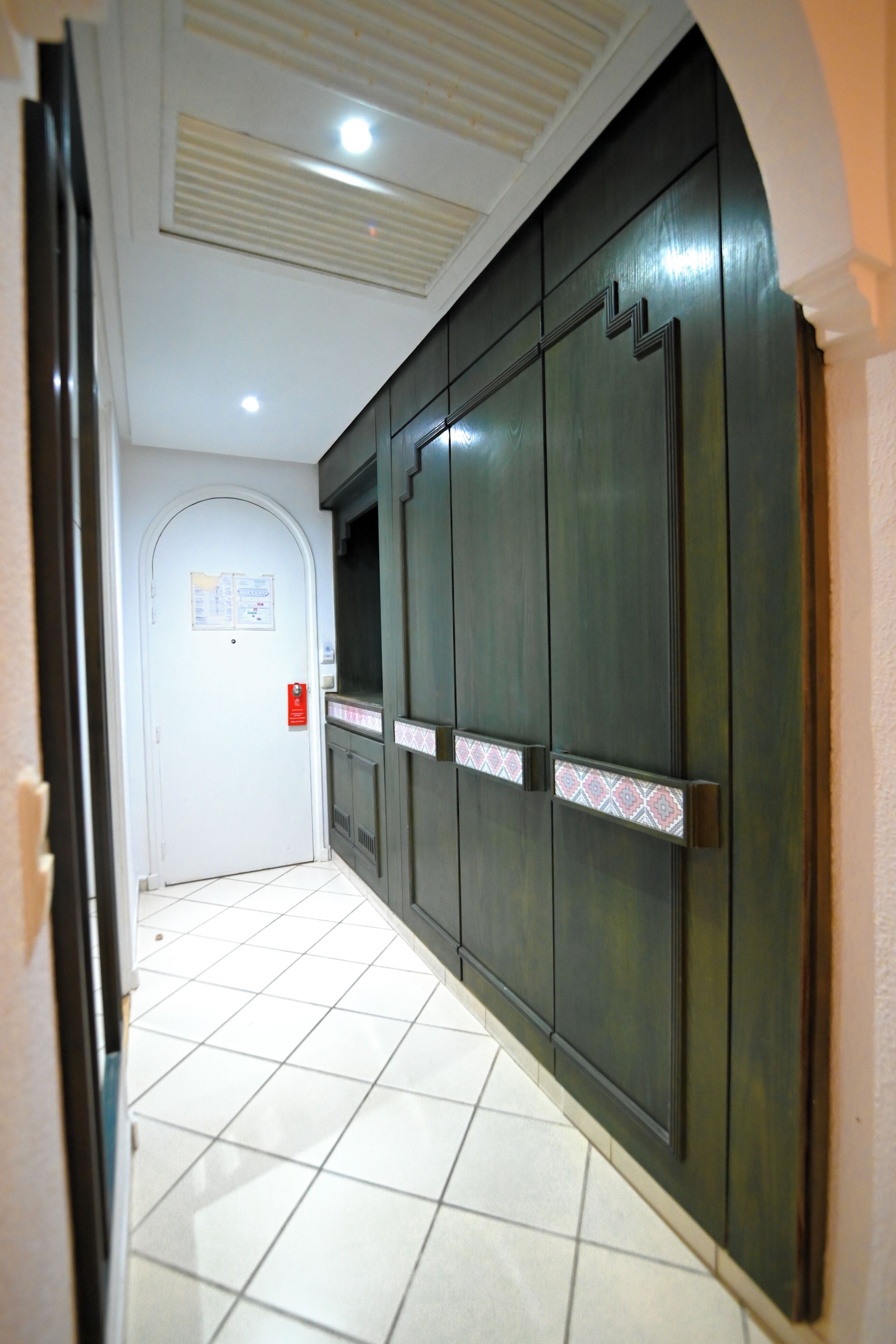 A corridor with a tiled floor, a door with a notice, and a large wardrobe with a patterned accent.