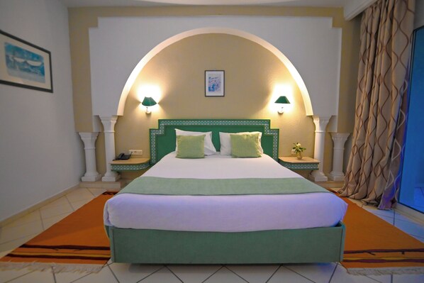 A hotel room with a large bed, two bedside lamps, a nightstand, a framed picture on the wall, and a curtain.