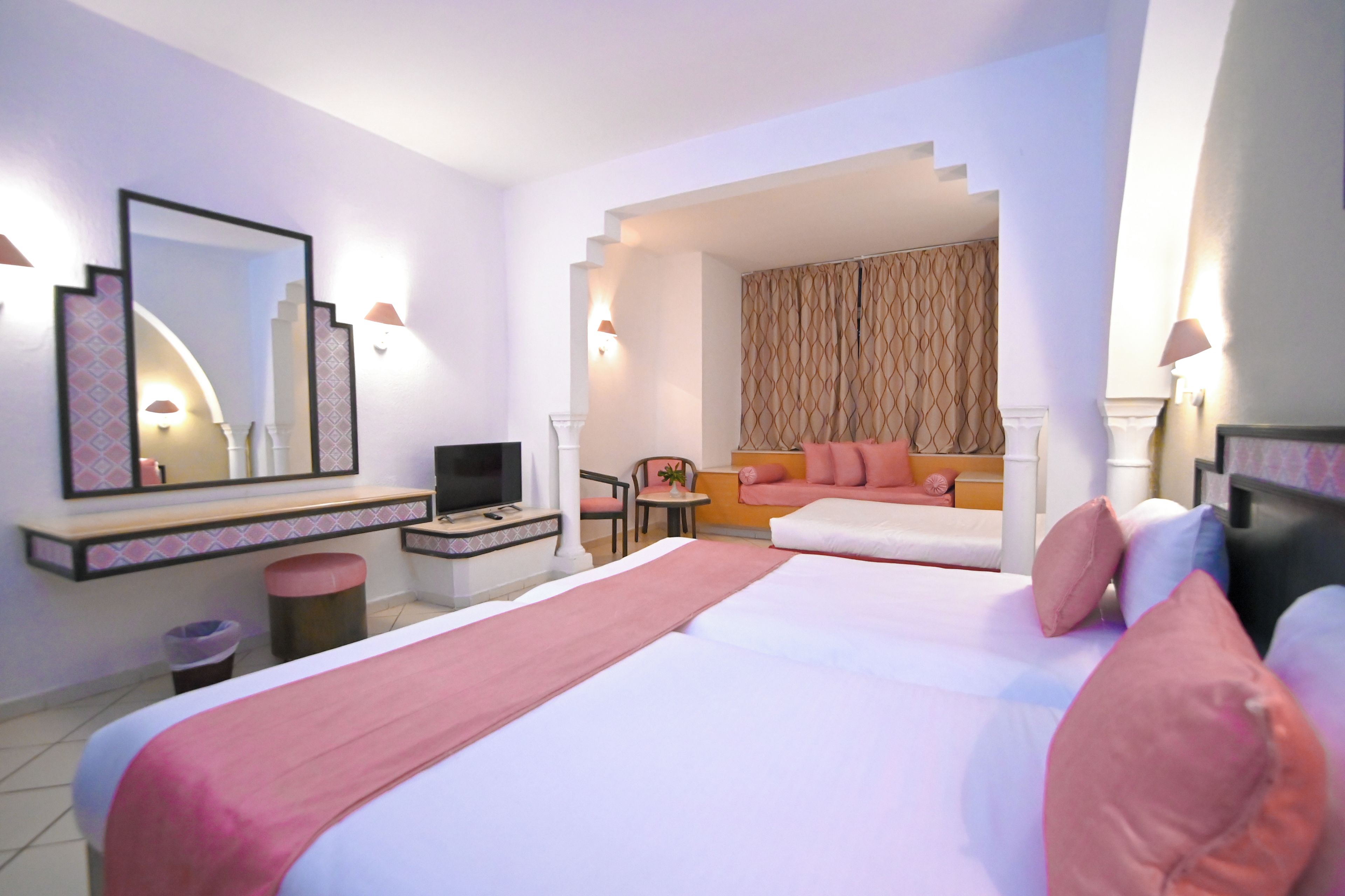 A hotel room with a large bed, a desk with a flat-screen TV, a chair, a small table, and a sofa.